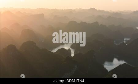 Blick aus der Vogelperspektive auf die nebelige, von Inseln übersäte Meereslandschaft der Ha Long Bay, umgeben von sanftem Sonnenschein, Hạ Long, Quang Ninh, Vietnam. Stockfoto