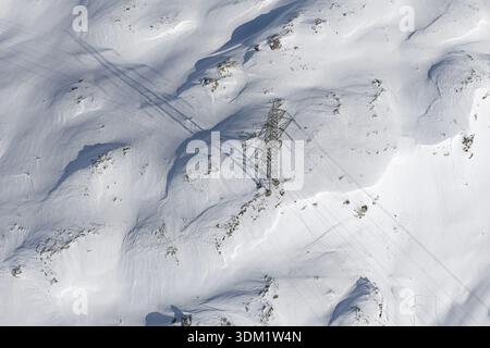 Aus der Vogelperspektive wirft ein hoch aufragendes Stromnetz-Pylon lange Schatten über die unberührte, schneebedeckte Landschaft Poschiavo, Graubünden, Schweiz Stockfoto