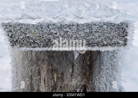 Komplizierte Frostkristalle bedecken eine Holzoberfläche und schaffen eine atemberaubende Winterszene voller eisiger Schönheit und ruhiger Gelassenheit. Stockfoto