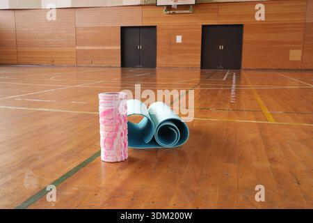 Eine blaue Yogamatte liegt auf dem Boden neben einer rosafarbenen. Die Matten werden aufgerollt und auf den Holzboden gestellt Stockfoto