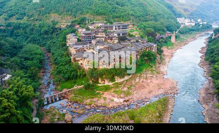 Die antike Stadt Bing’an in Guizhou, China, bietet traditionelle Holzpfahlhäuser entlang eines Flusstals und bewaldete Hügel. Stockfoto