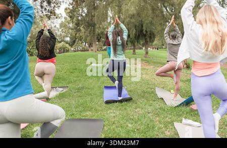 Frauen, die Yoga-Übungen im Freien im Stadtpark machen - gesundes Lebensstil und Sportkonzept - Hauptfokus auf zentrische Frau mit Flechtkörper Stockfoto
