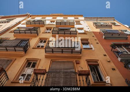 Flacher Blick auf ein Wohngebäude im Stadtzentrum von Valencia mit Balkonen, Fensterläden und einer warmen Fassade in klarem Blau Stockfoto