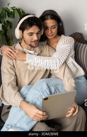 Ein junges Paar entspannt sich auf der Couch und lacht, während es zu Hause ein Tablet benutzt. Stockfoto