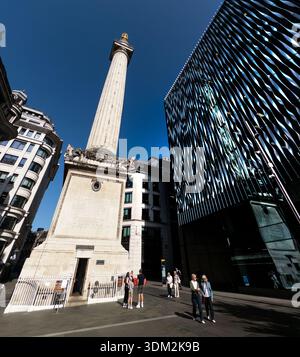 Die majestätische dorische Säule des Monuments to the Great Fire of London neben einem modernen welligen Glashochhaus, Touristen schlendern unter blauem Himmel Stockfoto