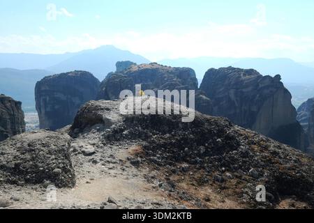 Person in gelber Jacke mit Panoramablick auf die Berglandschaft von Meteora, Griechenland Stockfoto
