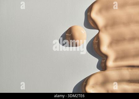 Beigefarbene flüssige Foundation, die auf weißer Oberfläche Flecken und kleine Tropfen erzeugt Stockfoto