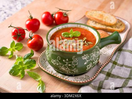 Rohe vegane Tomatensuppe in einer Schüssel mit Blumengeschirr, garniert mit Basilikum und Kürbiskernen auf Holzoberfläche Stockfoto