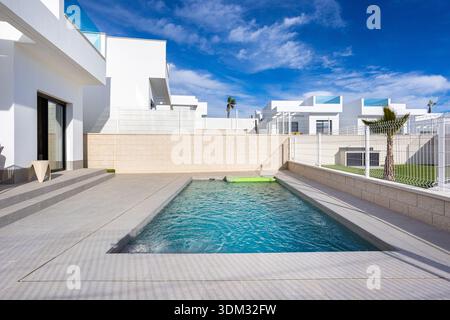 Sonnendurchfluteter Außenbereich mit rechteckigem Pool, sauberen Fliesen und heller weißer Villenfassade Stockfoto