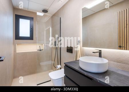 Elegantes Bad mit Glasdusche, Waschbecken, schwarzen Armaturen und warmen beigefarbenen Wänden Stockfoto