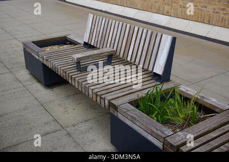 Leere Holzbank im Einkaufsviertel der Stadt. Öffentliche Sitzplätze mit Pflanzen Stockfoto