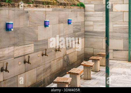 Ein traditioneller Waschbereich mit Marmorwänden, Messingwasserhähnen und Holzbänken im Innenhof der Moschee. Stockfoto