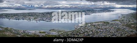 Panoramablick vom Storsteinen aus aus der Luft zeigt die Stadt Tromsø, die sich entlang des Fjords erstreckt und von schneebedeckten Bergen eingerahmt wird Stockfoto