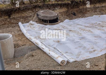 Dieses Bild zeigt eine Nahaufnahme der aktiven Bodenarbeiten mit einer Rolle weißen Geotextilen, die teilweise über eine Kies- und Schotteroberfläche verteilt ist Stockfoto