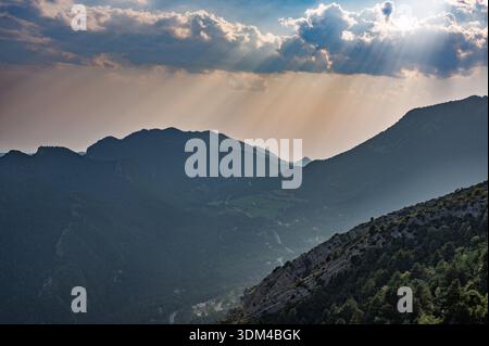 Dramatische Landschaft bei Sonnenuntergang über den Bergen von Berga, Katalonien, Spanien, mit intensiven, krepuskularen Sonnenstrahlen, die durch Wolken und Lichter durchdringen Stockfoto