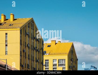 Moderne gelbe Apartmenthäuser vor blauem Himmel. Zwei senfgelbe Häuser mit schrägen Dächern in einem Viertel mit Wohnhochhäusern. Stockfoto