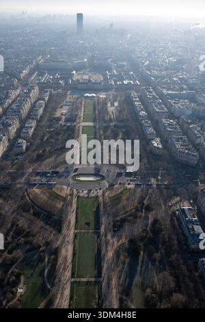 Hochwinkelansicht des Champ de Mars Parks in Paris. Urbane Gärten und Skyline der Stadt mit Montparnasse-Turm unter einem trüben Himmel an einem sonnigen Wintertag Stockfoto