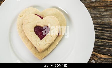 Zwei herzförmige Kekse mit Marmelade-Füllung auf einem weißen Teller Stockfoto