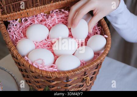 Osterfamilien-Traditionen. Unerkennbare Frau in Schürze, die die weißen Eier in den Korb legt und sich auf Ostern vorbereitet Stockfoto