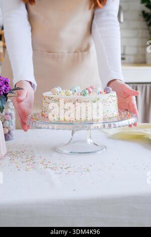 Frohe Ostern. Zugeschnittene Aufnahme einer Frau, die Osterkuchen in Pastellfarben in der Küche hält, sich auf den Urlaub vorbereitet, Kuchen mit süßen Eiern dekoriert || Model veröffentlicht Stockfoto