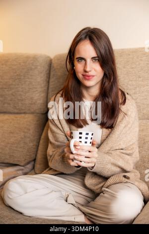 Frau, die auf der Couch sitzt und heißes Getränk trinkt Stockfoto
