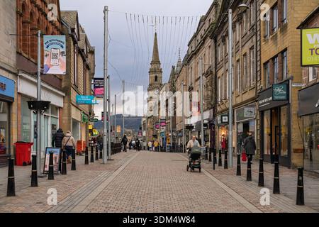 An einem bewölkten Februarnachmittag schlendern Fußgänger entlang einer Haupteinkaufsstraße in Inverness City, Highlands and Islands, Schottland. Läden Reihen sich an beide Seiten Stockfoto