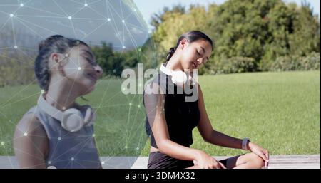 Sitzende Frau in schwarzer Activewear auf einer Bank auf dem Gras mit weißem Headset-Tracker-Knotenüberzug Stockfoto