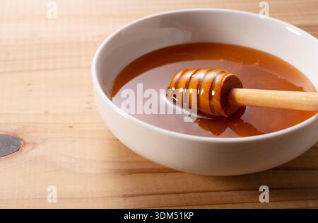 Hölzerner Honiglöffel in einer weißen Keramikschale, gefüllt mit dickem Manuka-Honig auf einem Holztisch. Stockfoto
