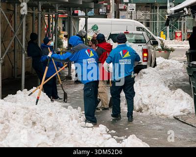 Die Arbeiter räumen den Schnee von einem Gehweg in Chinatown, Manhattan, New York City, nach einem Wintersturm, der sich entlang der Bordsteinkante stapelte Stockfoto