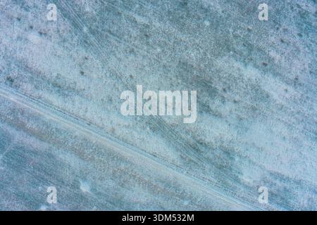 Ungleichmäßige Schneedecke auf dem dunklen Boden erzeugt einen dramatischen Kontrast zwischen weißem Eis und brauner Erde. Diese natürliche Abstraktion dient als Metapher für wechselnde Jahreszeiten oder globale Erwärmung. Stockfoto