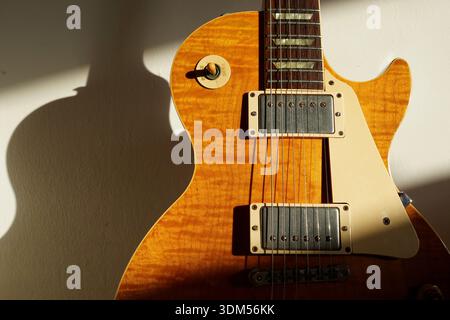Orangene elektrische Gitarre mit Sonnenschein an einer weißen Wand. Sonnenlicht leuchtet auf den Körper und erzeugt einen Schatten im Hintergrund Stockfoto