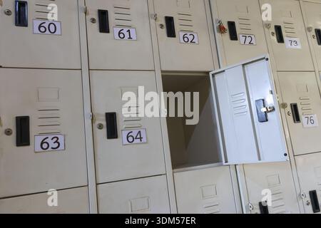 Geheimnisvoller offener Spind zwischen Reihen geschlossener Metallschränke im Schulflur. Ein leerer, dunkler Aufbewahrungsschrank schafft ein Gefühl von Leerstand und Geheimnissen im Inneren Stockfoto