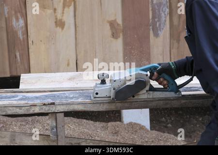 Fokussierter Zimmermann, der mit einem Hobel auf Holzdiele arbeitet. Fachhandwerker in der Werkstatt mit einem Elektrowerkzeug zur Holzglättung und Heimverbesserung Stockfoto