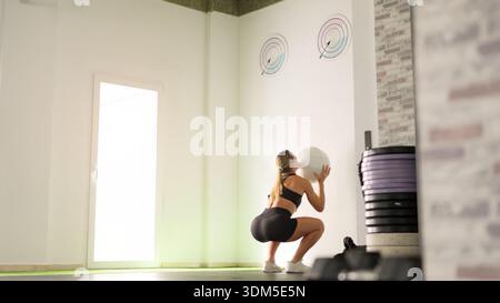 Frau, die im Fitnessstudio Medizin-Ball-Squat-Training macht Stockfoto