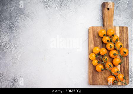 Gelbe Kirschtomaten auf Weinrebe auf hölzernem Schneidebrett über hellem texturiertem Hintergrund mit Kopierraum, frische Bio-Produkte. Stockfoto