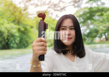Junge schöne asiatische Frau in der Tasche, Action-Kamera in der Natur im Freien, ideales Gerät für Reisevideos und Fotos. Stockfoto