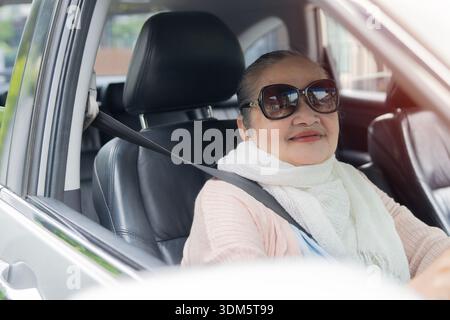 Porträt einer glücklichen Seniorin mit Sonnenbrillen-Fahrer, die aus dem Autofenster schaut. Das Konzept einer aktiven Person im Rentenalter Stockfoto