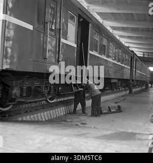 Slawjansk, Region Donezk, ukrainische SSR, UdSSR. 1970er Jahre Eine authentische Archivansicht von Eisenbahnmechanikern, die in einer Betriebswerkstatt an einem elektrischen Vorortzug warten. Zwei Arbeiter in Schutzkleidung untersuchen das Laufwerk und die Stufen des Personenwagens, die über einer gefliesten Inspektionsgrube stehen. Das Bild erfasst die technischen Details des rollenden Materials, den Radsatz mit Federn, den täglichen Reparaturprozess und die industrielle Atmosphäre der Transportanlage im friedlichen Donbass. Stockfoto