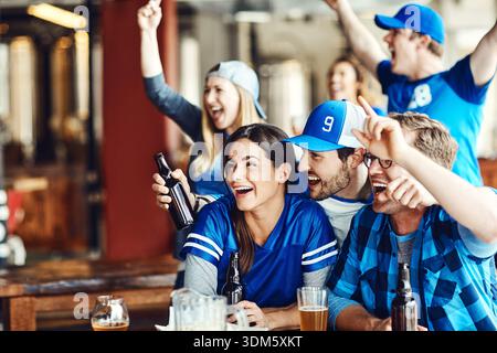 Genießen Sie ein paar Biere, während Sie unser Lieblingsteam anfeuern. Eine Gruppe von aufgeregten Freunden, die ihr Lieblingsteam an der Bar anfeuern. Stockfoto