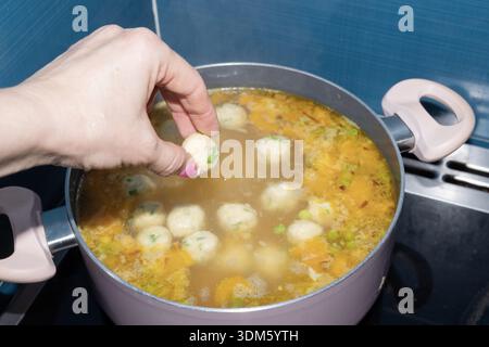Hausgemachte Suppe mit Knödeln, die in einem Topf auf dem Herd gekocht werden. Traditionelle Küchenszene mit warmer Brühe, Gemüse und einfachen Gerichten. Stockfoto