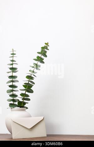 Minimales Stillleben mit Eukalyptuszweigen und Kuvert auf Holztisch Stockfoto