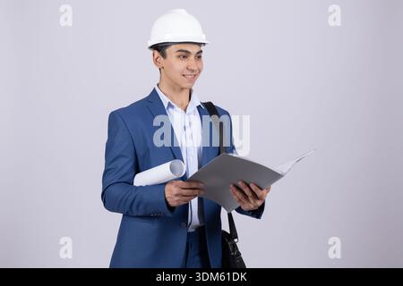 Junger Mann in blauem Anzug und weißem Hardhat, der einen Plan hält Stockfoto