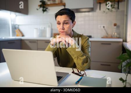Eine nachdenkliche, verärgerte Geschäftsfrau mit professionellem Burnout arbeitet von zu Hause aus auf dem Notebook. Stockfoto