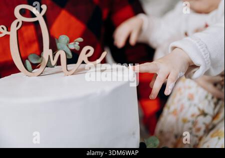 Baby-Finger-Verkostung Frosting auf der ersten Geburtstagskuche mit einem Topper, Großaufnahme Stockfoto