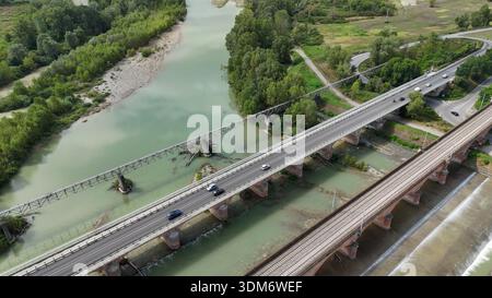Aus der Vogelperspektive zweier getrennter Brücken, eine für den Straßenverkehr und eine für die Züge, die den Trebbia-Fluss in der Emilia Romagna, Italien, überspannen Stockfoto