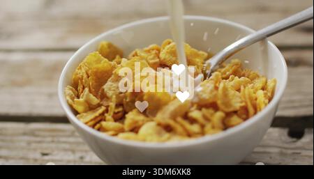 Weiße Keramikschale mit Cornflakes, die Milch auf rustikalen Tischplatten, Löffel und Herz-Bokeh gießt Stockfoto