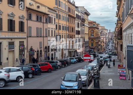 18. Januar 2026, Rom, Italien: Geparkte Autos säumen eine enge Straße aus pastellfarbenen Wohnhäusern, während Fußgänger durch ein Wohnviertel, Sho, fahren Stockfoto