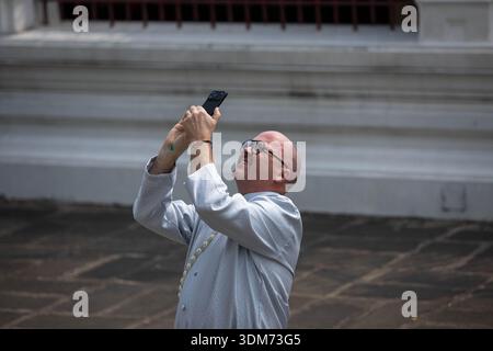 BANGKOK, THAILAND, 15. JAN 2026: Mann in traditioneller thailändischer Kleidung, schaut beim Fotografieren nach oben, Glatzkopf, männliche Hautstruktur, Nahaufnahme, im Wat Arun Stockfoto