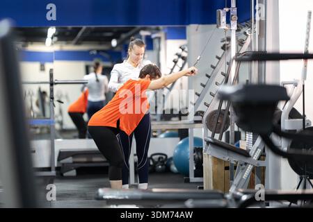 Frau, die mit Personal Trainer auf Kabel-Pulldown-Maschine trainiert Stockfoto