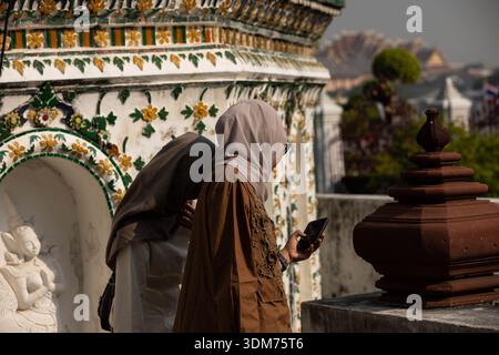 Zwei weibliche Touristen, die Fotos auf dem Smartphone überprüfen und im Wat Thair, Seitenprofil, im Wat Arun erkunden. Stockfoto